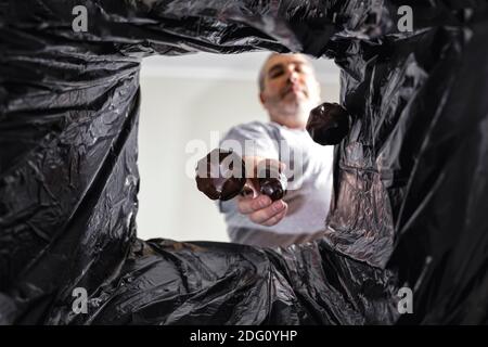 un homme en surpoids jette des bonbons dans les poubelles. vue depuis le sac poubelle. perte de poids et saine alimentation Banque D'Images