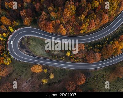 Vue aérienne de la route rurale avec voiture blanche dans les forêts d'automne jaune et orange. Vue de dessus .capturé par dessus avec drone. Banque D'Images