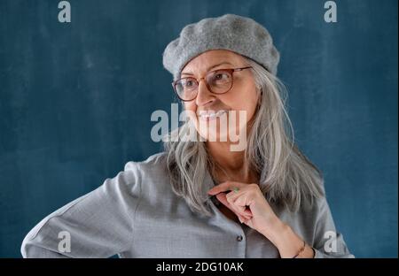 Portrait d'une femme âgée avec un béret gris debout à l'intérieur sur fond sombre. Banque D'Images