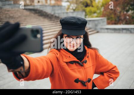 Une jeune femme portant un manteau et un chapeau prend une photo d'elle-même sur téléphone mobile dans la rue Banque D'Images