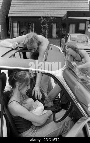 Milton Keynes Buckinghamshire 1970s couple professionnel de classe moyenne en dehors de leur nouvelle maison moderne sur un nouveau développement de logement. Le père va toucher son nouveau bébé, la mère regarde dessus. Bébé étant tenu par une petite amie qui est à la journée pour voir la nouvelle maison et le bébé. Traîner près de la voiture de famille qui est garée à côté de leur maison. 1977 HOMER SYKES Banque D'Images