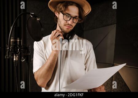 Jeune homme confiant chanteur lisant attentivement le texte de la nouvelle chanson travailler dans un studio d'enregistrement sonore Banque D'Images
