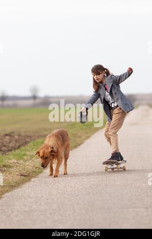 Une fille sur un skateboard est tirée par un chien Banque D'Images