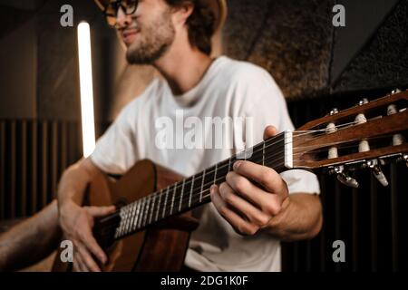 Gros plan jeune musicien masculin attrayant jouant avec confiance à la guitare en studio d'enregistrement Banque D'Images