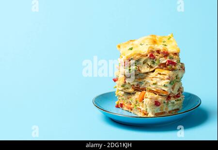 Lasagnes aux légumes avec sauce blanche, grande portion sur l'assiette, sur fond bleu. Cuisine italienne maison. Plat végétarien avec petits pois, carottes et fromage Banque D'Images