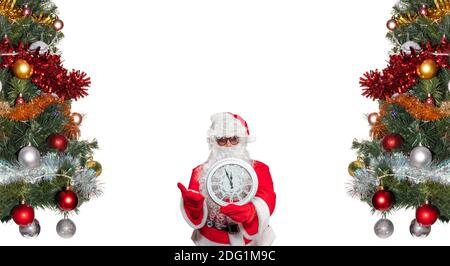 Le Père Noël tient une horloge blanche qui indique cinq minutes à minuit. Le Père Noël est entouré d'arbres de Noël décorés. Concept de la veille du nouvel an. Copier Banque D'Images
