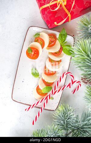 Salade Caprese de Noël en forme de Candy Cane, Mozzarella et tomates sur l'assiette servi pour le nouvel an et Noël, avec décor de Noël sur table blanche Banque D'Images