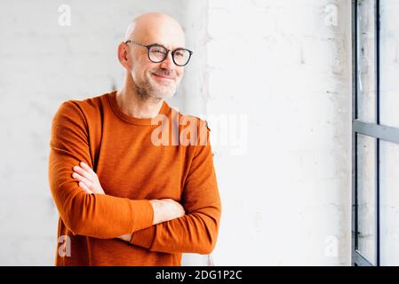 Portrait d'un homme âgé souriant debout à l'intérieur et regardant par la fenêtre. Banque D'Images