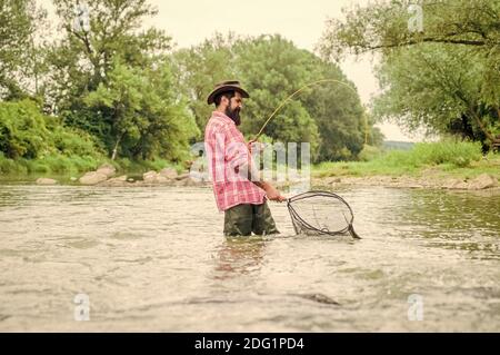 week-end d'été. Pêche au gros gibier. Pêcheur barbu dans l'eau. Activités de loisir et de sport. Pothunter. Homme mature pêche à la mouche. Homme attrapant le poisson. Pêcheur avec canne à pêche. Le vieil homme et la mer. Banque D'Images