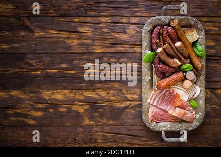 Divers types de charcuterie appétissante disposés sur un plateau élégant, arrière-plan, table en bois ancienne avec un espace vide pour une inscription Banque D'Images