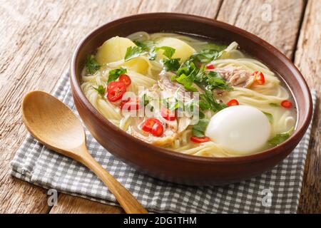 Nourriture péruvienne Caldo de Gallina poulet soupe de nouilles avec oeuf bouilli et herbes gros plan dans une assiette sur la table. Horizontale Banque D'Images