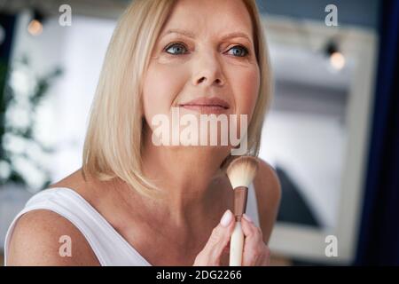 Femme âgée appliquant du maquillage dans la salle de bains Banque D'Images