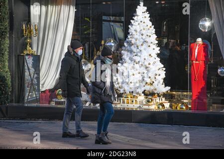 Couple portant des masques protecteurs dans la ville à proximité d'un magasin ou centre commercial pendant Noël, Covid ou épidémie de coronavirus Banque D'Images