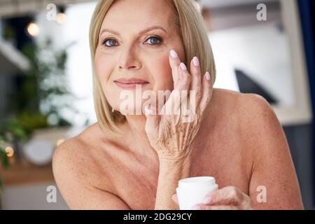 Femme âgée utilisant de la crème anti-rides dans la salle de bains Banque D'Images