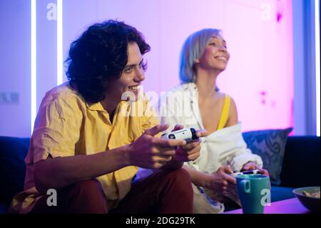 Couple jouant au jeu vidéo sur la console. Fille perdant et ne laissant pas le gars jouer normalement en fermant ses yeux avec sa main. S'amuser ensemble à la maison Banque D'Images