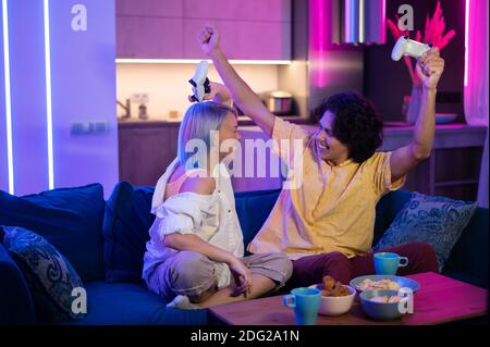 Joyeux petit ami et petite amie jouant à des jeux vidéo et tenant des joysticks à la maison. Couple du millénaire qui profite du jeu tout en étant assis sur un canapé et en dépensant Banque D'Images