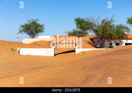 Porte d'entrée blanche enterrée dans le sable du village fantôme d'Al Madame, avec des dunes de sable et des arbres de ghaf sauvages. Banque D'Images