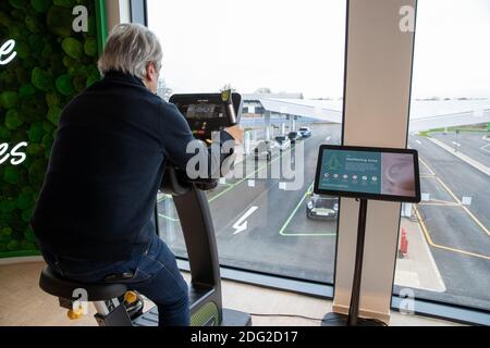 La photo du 2020 décembre montre un conducteur sur une moto d'exercice au premier piste électrique du Royaume-Uni à Braintree, dans l'Essex., qui aide à charger sa voiture. La première piste électrique du Royaume-Uni a ouvert ses portes aujourd’hui – avec la possibilité de charger des voitures en seulement 20 minutes. Le site de Braintree, dans l'Essex, est le premier d'environ 100 forecourts électriques construits dans tout le pays au cours des cinq prochaines années dans le cadre d'un programme de 1 milliard de livres sterling. Elle devait ouvrir en novembre, mais elle a été retardée en raison de la pandémie du coronavirus et du deuxième confinement national. Banque D'Images