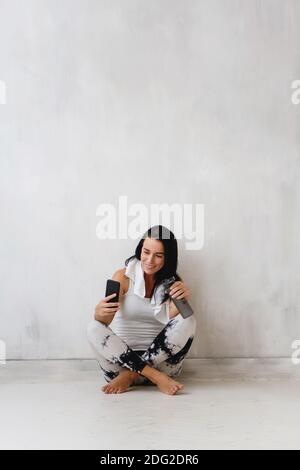 Belle femme sportive assise sur le sol et faisant selfie après l'entraînement sur le fond de mur blanc. Banque D'Images