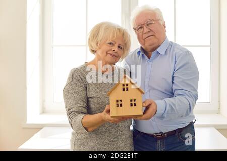 Heureux couple senior tenant une petite maison debout près de la fenêtre dans leur nouvelle maison Banque D'Images