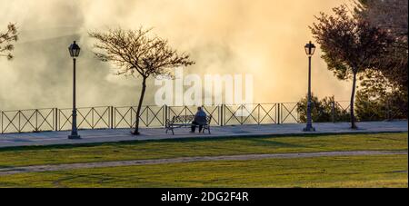 Silhouette d'un homme assis sur un banc de parc un spectaculaire coucher de soleil d'hiver Banque D'Images