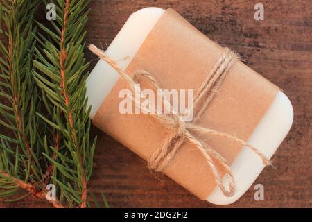 Barre de savon de conifère naturel fait main enveloppée de papier artisanal, et branche de sapin sur table en bois. Cadeau de Noël écologique. Banque D'Images