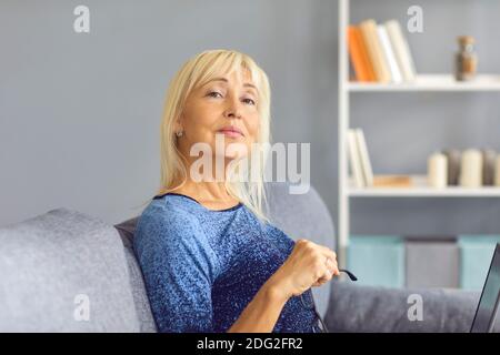 Femme mûre sérieuse assise sur le canapé et regardant loin comme si vous écoutez quelqu'un Banque D'Images