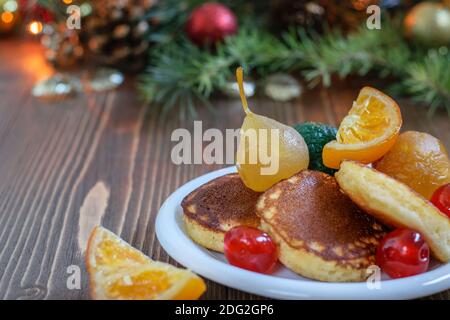 Crêpes japonaises moelleuses avec fruits espagnols sur la plaque blanche, sur le fond de Noël en bois de la maison. Petit déjeuner sain et festif, vue latérale. Banque D'Images