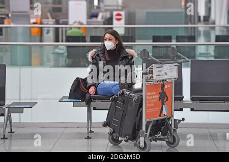 Voyages à thème en période de pandémie de corona. Jeune femme avec masque, masque avec sa valise, bagages à l'aéroport de Munich le 6 décembre 2020. Assis dans le terminal, hall des départs, en attente du départ. MODÈLE DISPONIBLE ! | utilisation dans le monde entier Banque D'Images