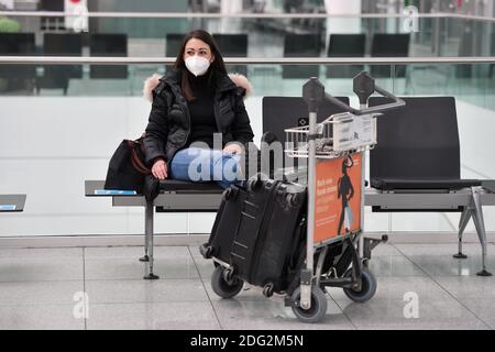 Voyages à thème en période de pandémie de corona. Jeune femme avec masque, masque avec sa valise, bagages à l'aéroport de Munich le 6 décembre 2020. Assis dans le terminal, hall des départs, en attente du départ. MODÈLE DISPONIBLE ! | utilisation dans le monde entier Banque D'Images