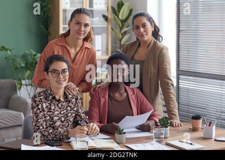 Groupe multiethnique de quatre femmes d'affaires contemporaines souriant à la caméra poser au bureau Banque D'Images