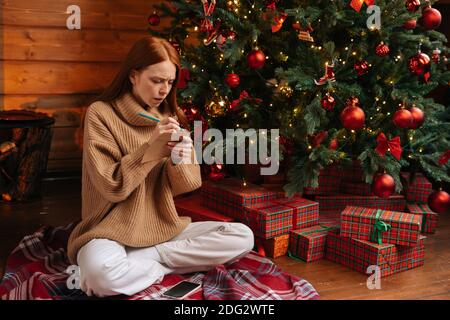 Jeune femme rêveuse écrivant la lettre de Noël au Père Noël assis sur fond d'arbre de Noël. Banque D'Images