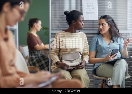 Portrait de deux femmes ethniques bavardant activement en attendant en file d'attente pour un entretien d'emploi au bureau, espace de copie Banque D'Images