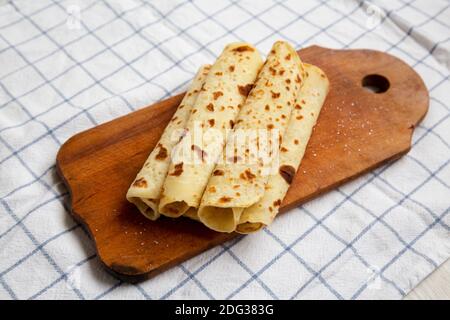 Pain plat de pommes de terre norvégien (Lefse) fait maison avec beurre et sucre sur une planche de bois rustique sur tissu, vue latérale. Banque D'Images