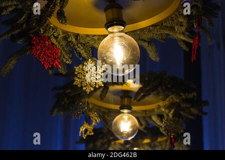 Lustre avec ampoules lumineuses décorées de façon saisonnière pour Noël flocons de neige jaunes et rouges et branches de pin sur un bleu arrière-plan Banque D'Images