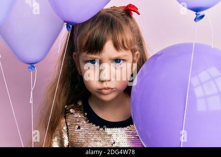 Petite fille caucasienne de tenir des ballons sceptique et nerveux, frowning bouleversé à cause du problème. Personne négative. Banque D'Images