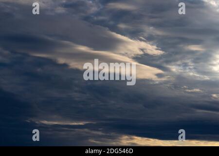 As a storm builds, layered stratus clouds are illuminated by a setting November sun Stock Photo