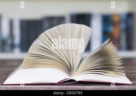 Livre ouvert devant la bibliothèque avec des pages volantes et un flou de mouvement avec une mise au point sélective. Banque D'Images