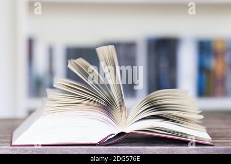 Livre ouvert devant la bibliothèque avec des pages volantes et un flou de mouvement avec une mise au point sélective. Banque D'Images