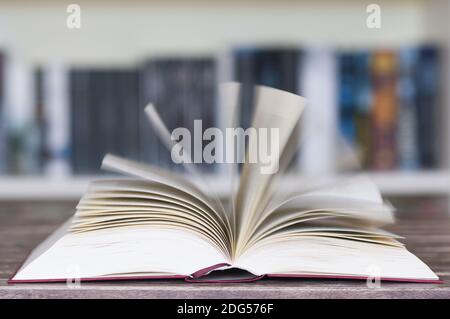 Livre ouvert devant la bibliothèque avec des pages volantes et un flou de mouvement avec une mise au point sélective. Banque D'Images