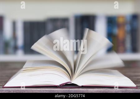 Livre ouvert devant la bibliothèque avec des pages volantes et un flou de mouvement avec une mise au point sélective. Banque D'Images