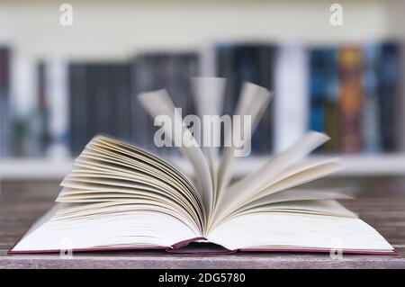 Livre ouvert devant la bibliothèque avec des pages volantes et un flou de mouvement avec une mise au point sélective. Banque D'Images