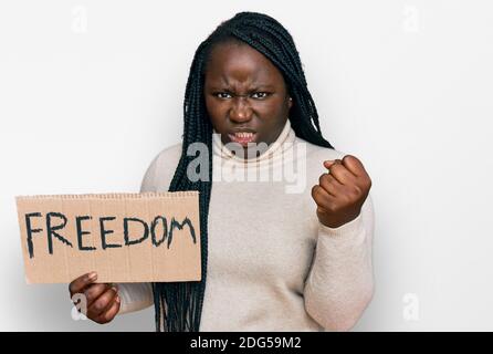 Jeune femme noire avec des tresses tenant la bannière de liberté ennuyée et frustrée criant avec la colère, hurlant fou avec la colère et la main levée Banque D'Images