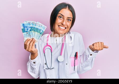 Belle femme hispanique portant un uniforme médical tenant 20 dollars de hong kong criant fier, célébrant la victoire et le succès très excité avec l'augmentation Banque D'Images