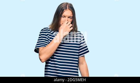 Beau caucasien avec de longs cheveux portant un t-shirt rayé décontracté qui sent quelque chose de stinky et dégoûtant, une odeur intolérable, qui retient l'haleine Banque D'Images