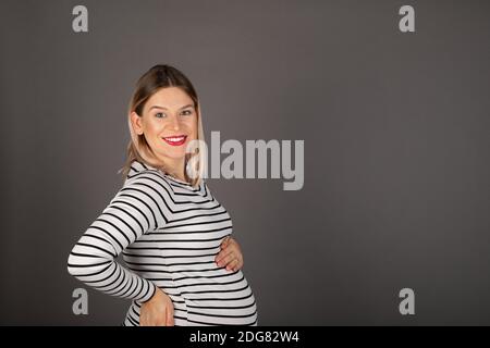 Jeune femme enceinte caucasienne au troisième trimestre posant devant d'arrière-plan gris Banque D'Images