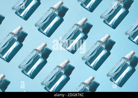 Tendance modèle de vaporisateurs avec antiseptique alcoolique, assainisseurs sur un fond bleu. Couché à plat, ombre dure du soleil. Concept de protection antivirus Banque D'Images