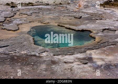 Le geyser de dépression a un bord festonné, l'eau bleue avec les dépôts de formation de minéraux à différents niveaux d'eau créant une lèvre épaisse de dépôt de fritté. Banque D'Images