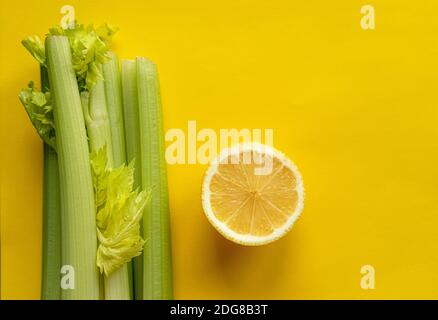 Une tranche de citron et un bouquet de céleri se trouvent sur fond jaune Banque D'Images