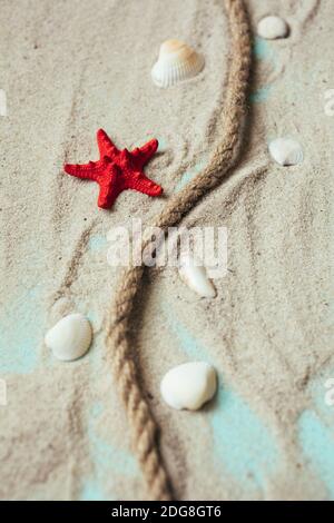 Corde d'amarrage, coquillages et étoiles de mer rouges sur sable sur fond de table en bois bleu. Concept de voyage en mer. Banque D'Images